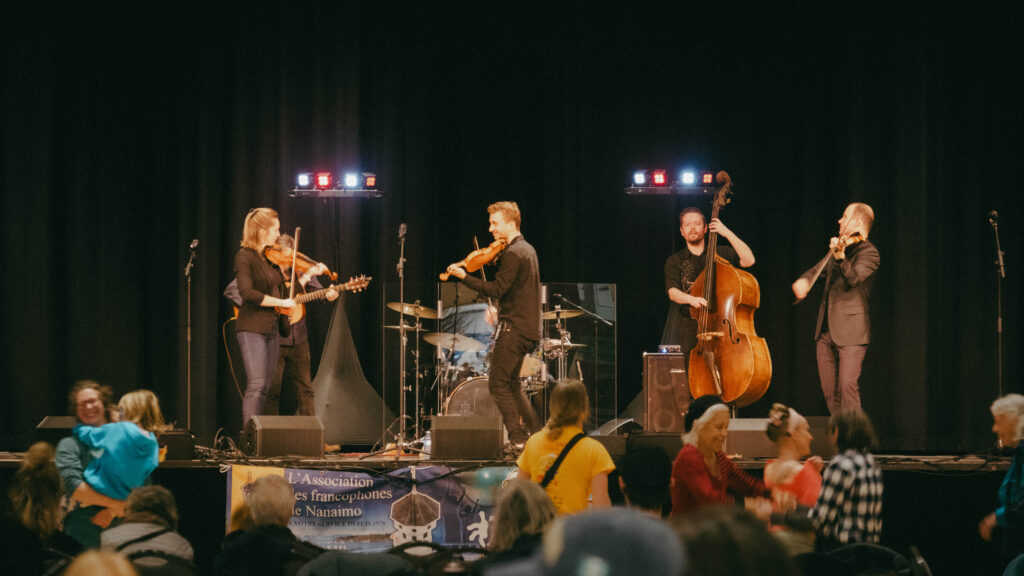 General view of the Maple Sugar Festival showing people at tables, musicians on stage, and dancers smiling, capturing the festival’s music, workshops, and community fun.