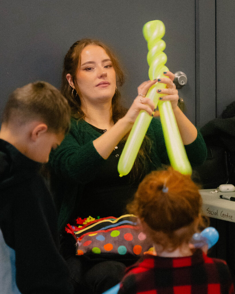 Photo of an artist twisting a balloon while two kids watch in awe.