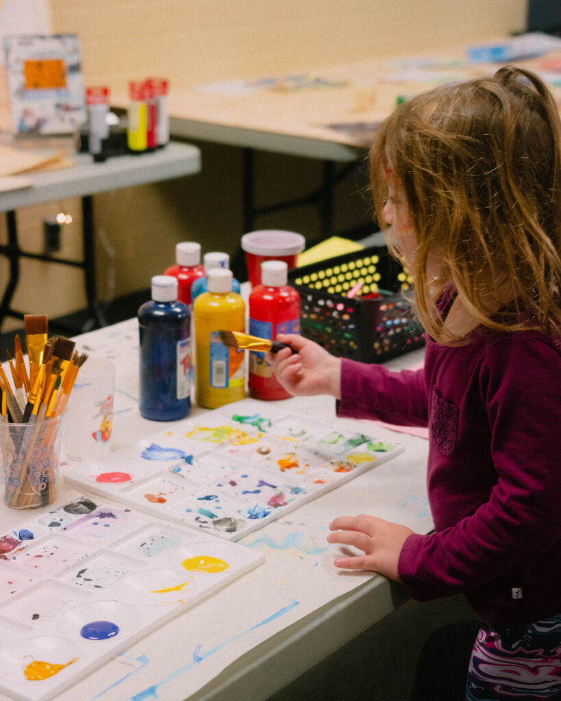 Photo of a child sitting at tables, drawing and crafting in a quiet, guided space, during the Maple Sugar Festival family activities.